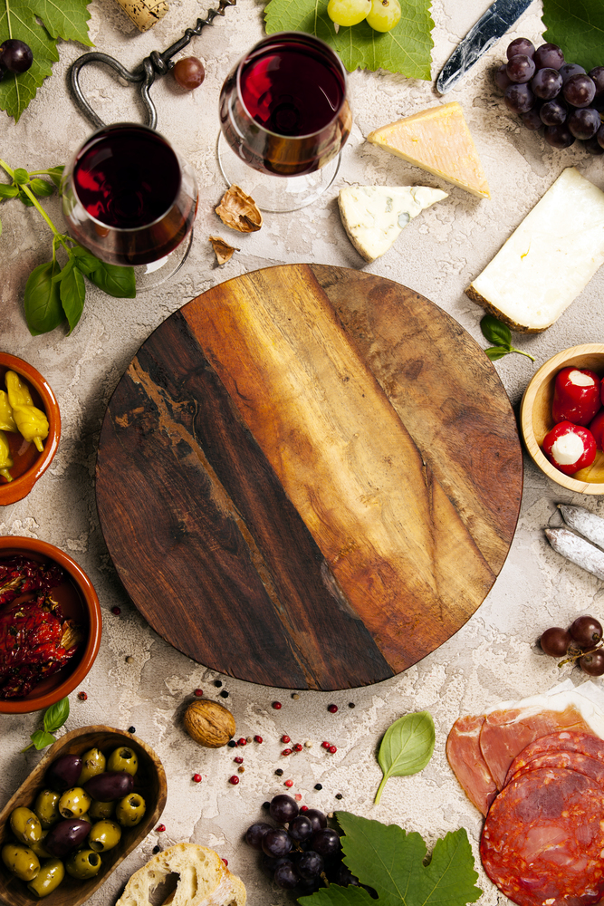 Wine and snack set. Variety of cheese, mediterranean olives, prosciutto,baguette slices, black and green grapes, sun-dried tomatoes, peppers and glasses of red wine over grey marble background, top view, copy space