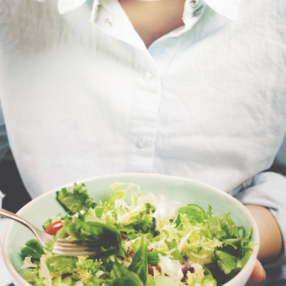 Fresh summer salad in bowl with lettuce, tomatoes, onions and cucumbers. Girl in jeans and blue shirt holding fork, top view. Clean eating, dieting food concept