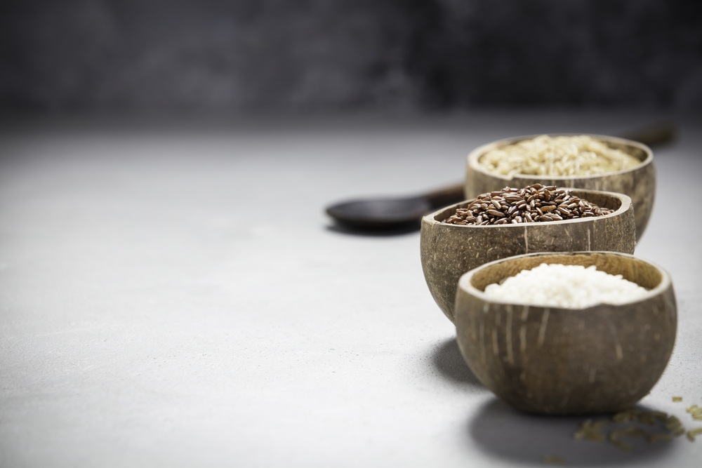 Assortment of different rice in bowls: Rice berry, Brown rice and Risotto rice on grey concrete background.