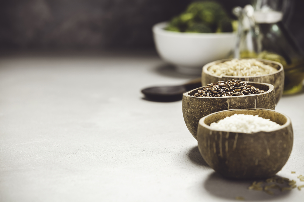 Assortment of different rice in bowls: Rice berry, Brown rice and Risotto rice and cooking ingredients  on grey concrete background. Clean eating