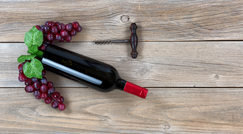Overhead view of Red wine bottle with grapes and corkscrew on weathered wooden boards