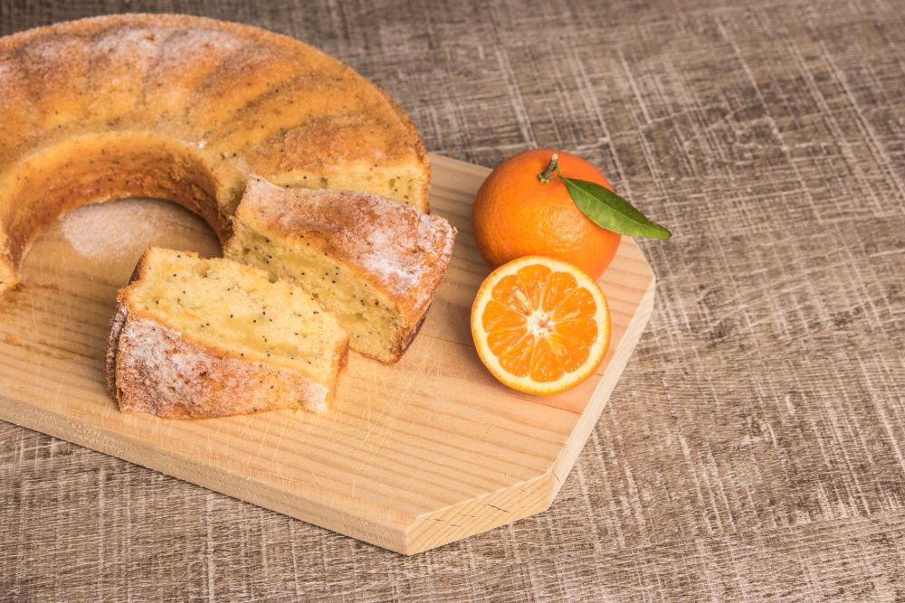 Slices of clementine cake with powdered sugar topping. Cake on a board with fresh clementines on wooden board.