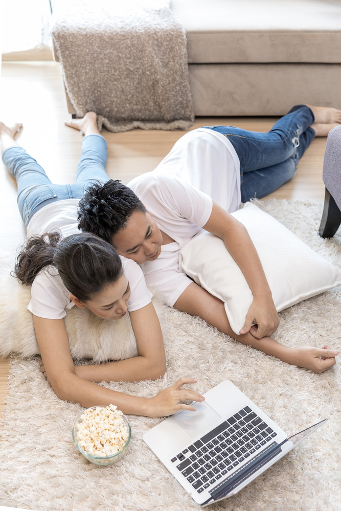 Young Asian Couples lying down and using laptop together in living room of contemporary house for modern lifestyle concept