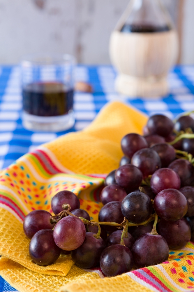 Closeup of a bunch of red grapes and a glass of red wine with a wine flask on background over a checkered tablecloth. Closeup of a bunch of red grapes and a glass of red wine with a wine flask