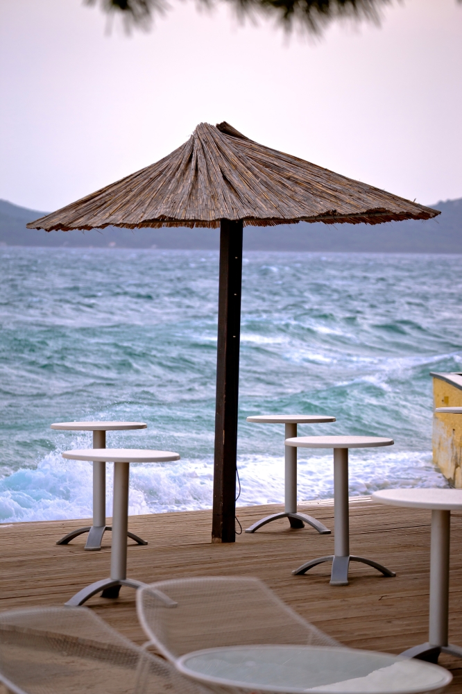 Beach bar parasol by rough sea vertical view, Zadar, Croatia