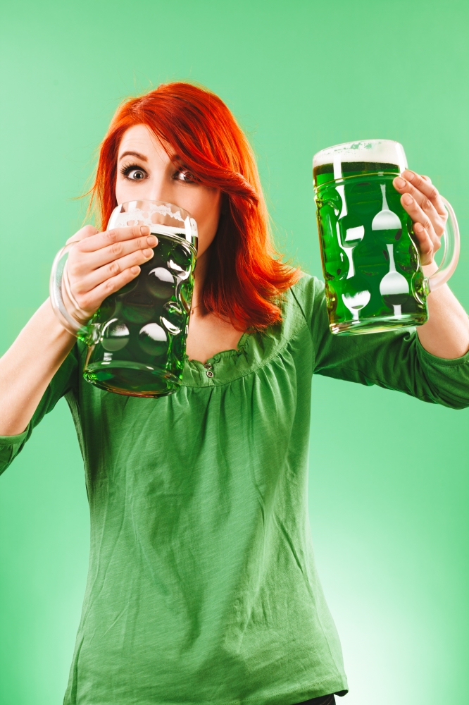 Photo of a beautiful redhead woman holding and drinking two huge green beers.