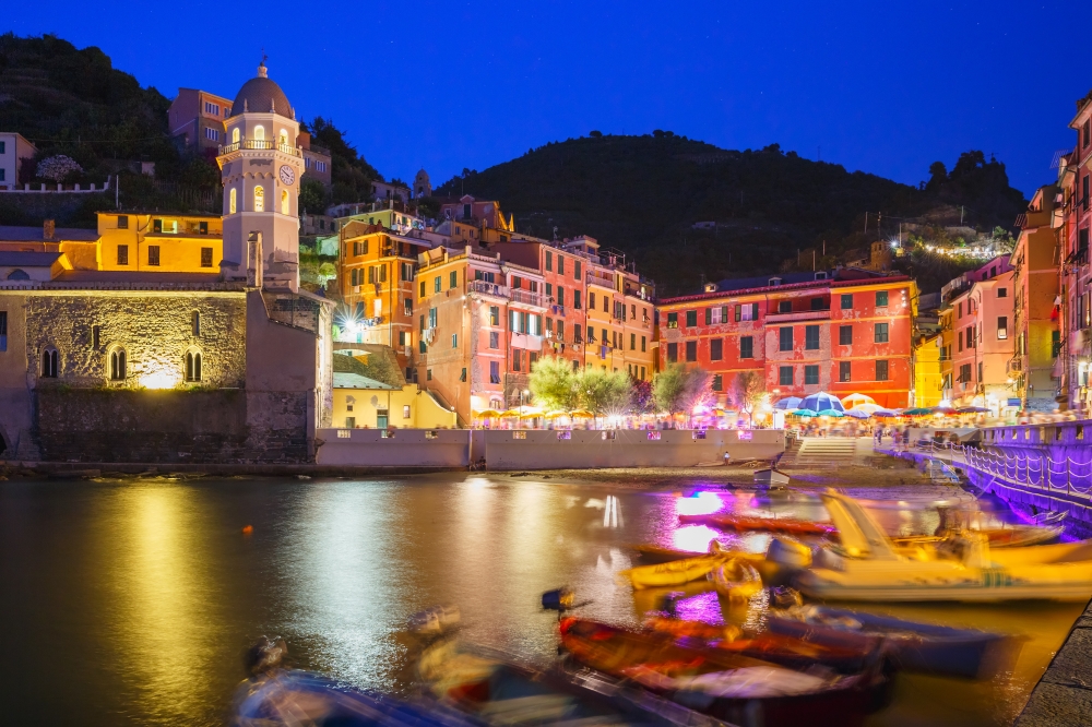 Night fishing village Vernazza with Santa Margherita di Antiochia Church, Five lands, Cinque Terre National Park, Liguria, Italy. Boats blurred motion on the foreground.
