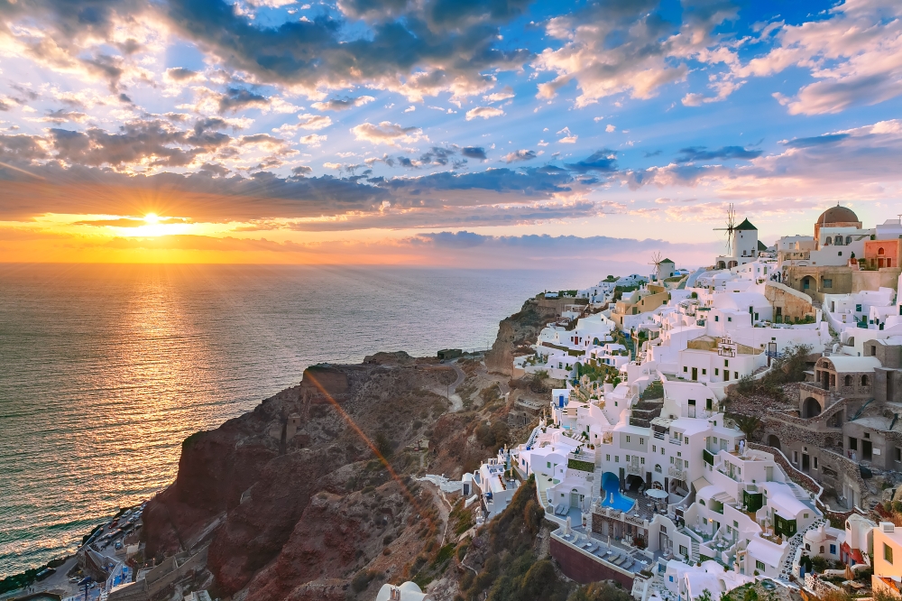 Oia or Ia at sunset, Santorini, Greece. Picturesque view, Old Town of Oia or Ia on the island Santorini, white houses, windmills and church with blue domes at sunset, Greece