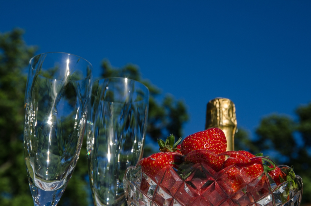 Celebration with a bottle of champagne, two glasses and a bowl with strawberries outdoors by blue sky