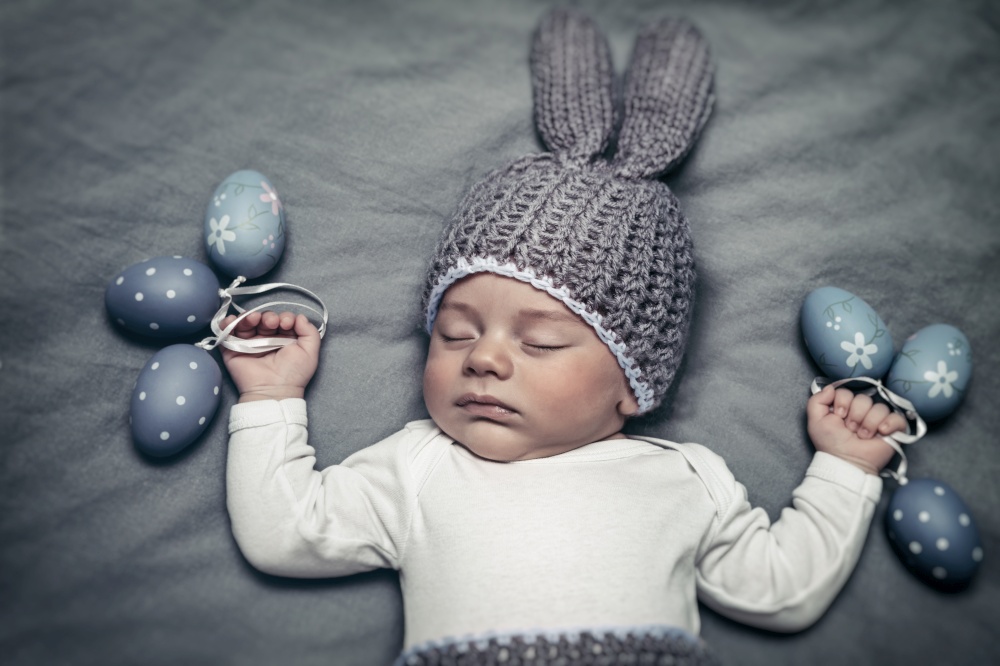 Portrait of a cute little baby boy wearing bunny costume and holding decorative eggs in hands, happy Easter holiday