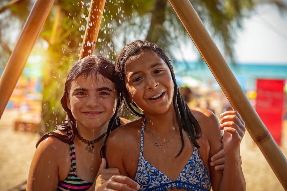 Portrait of a two happy little girls standing together under the shower on the beach, best friends with pleasure spend summer holidays near the sea