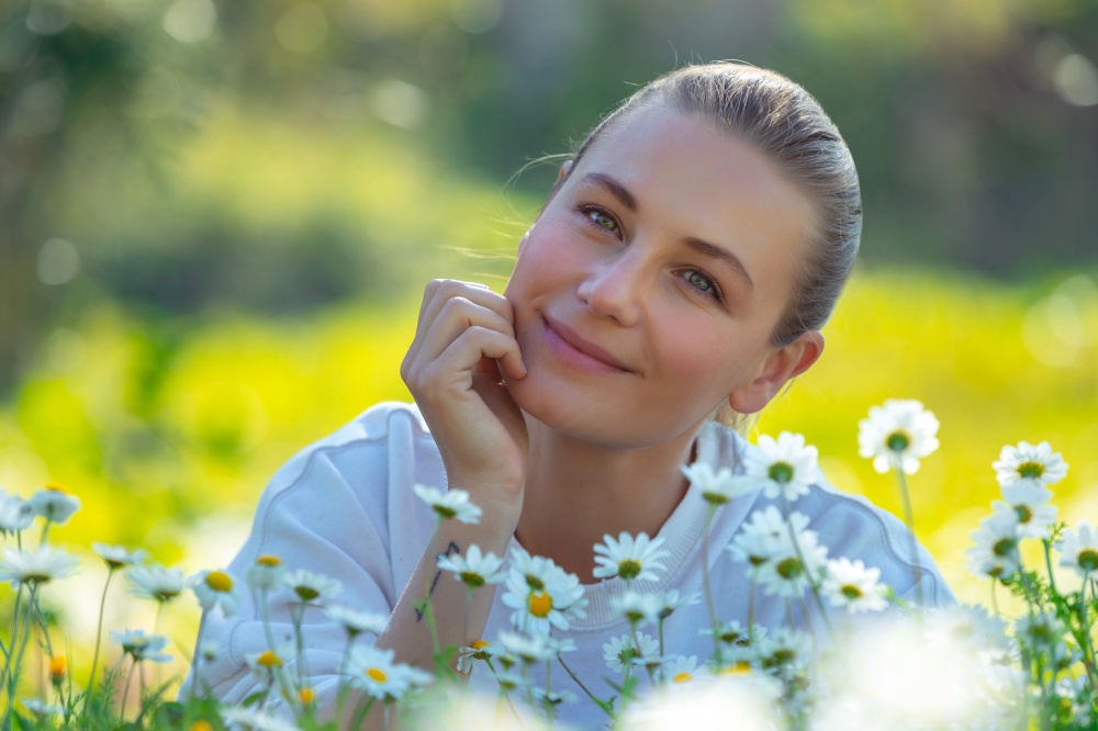 Portrait of a beautiful young woman with pleasure spending time outdoors, enjoying fresh daisy flowers on the floral meadow, happy spring holidays in countryside