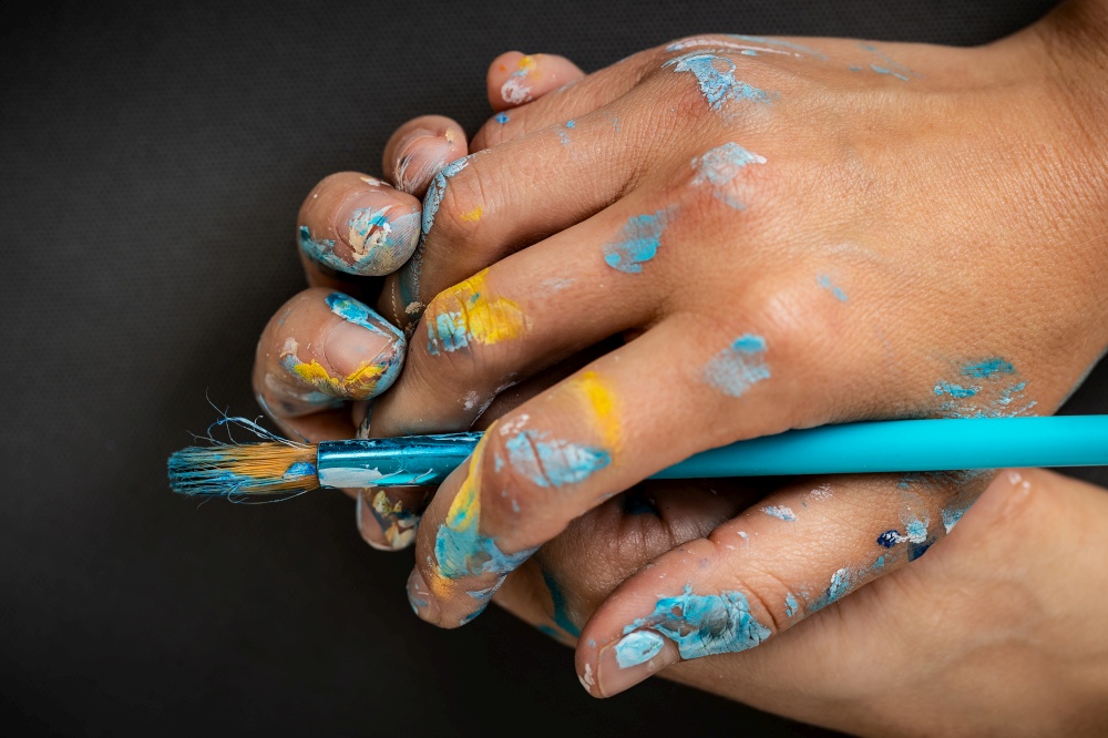 Close Up photo of a paint-stained painters hands holding paintbrush, conceptual photo of a creativity and idea generation