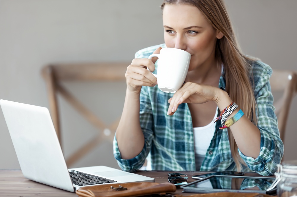 Beautiful Young Woman Working from Home. Pretty Female with Pleasure Drinking Coffee and Working on the Laptop. Freelancing.