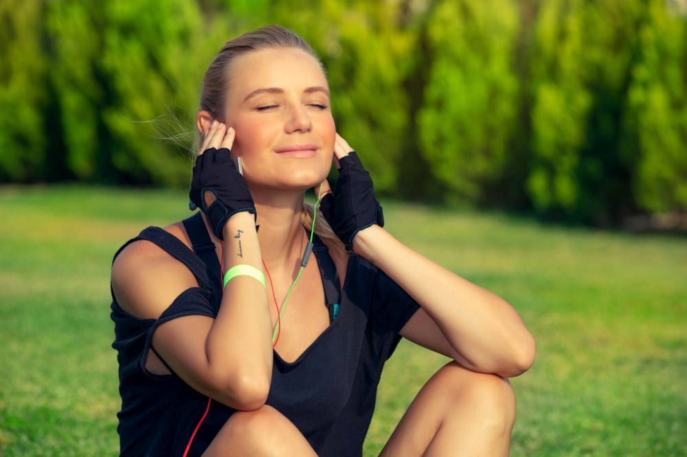 Beautiful fit girl relaxing after good workout, enjoying sun lights with closed eyes, tanning and listening music, meditation outdoors, harmony and soul balance concept