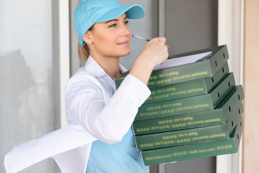 Nice Delivery Girl Wearing Special Uniform Signs a Check for Payment. Delivering Hot Delicious Pizza. Delivery Door to Door. Conceptual Photo of a Service Occupation.