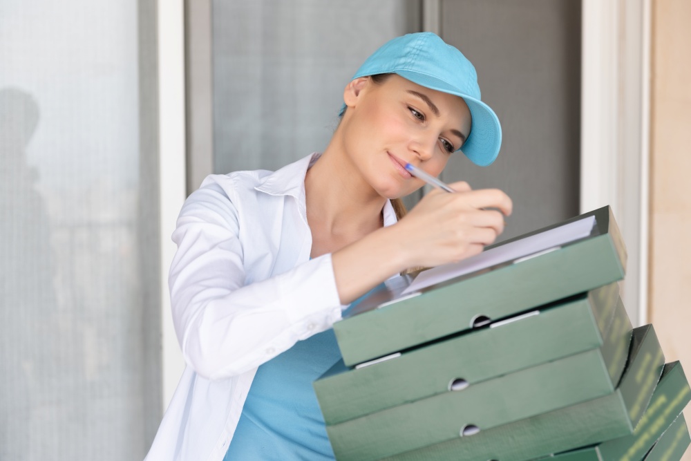 Nice Delivery Girl Wearing Special Uniform Signs a Check for Payment. Delivering Necessary Products. Modern Online Business. Conceptual Photo of a Service Occupation.
