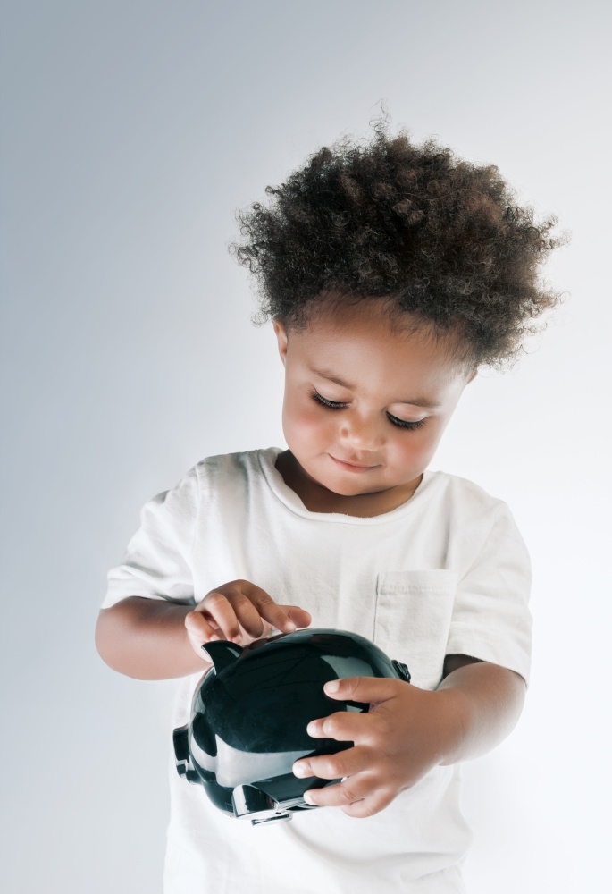 Portrait of a Nice African American Child Putting Coins in to the Pig-shaped Money Box Isolated on Grey White Background. Investment in to the Future