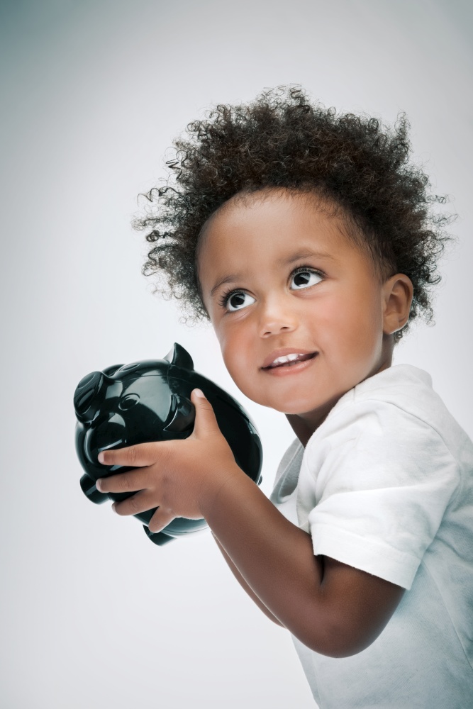 Portrait of a Cute Little African American Boy Shakes his Piggy Bank and Checks How Many Coins he Has. Isolated on Grey White Background. Happy Childhood.