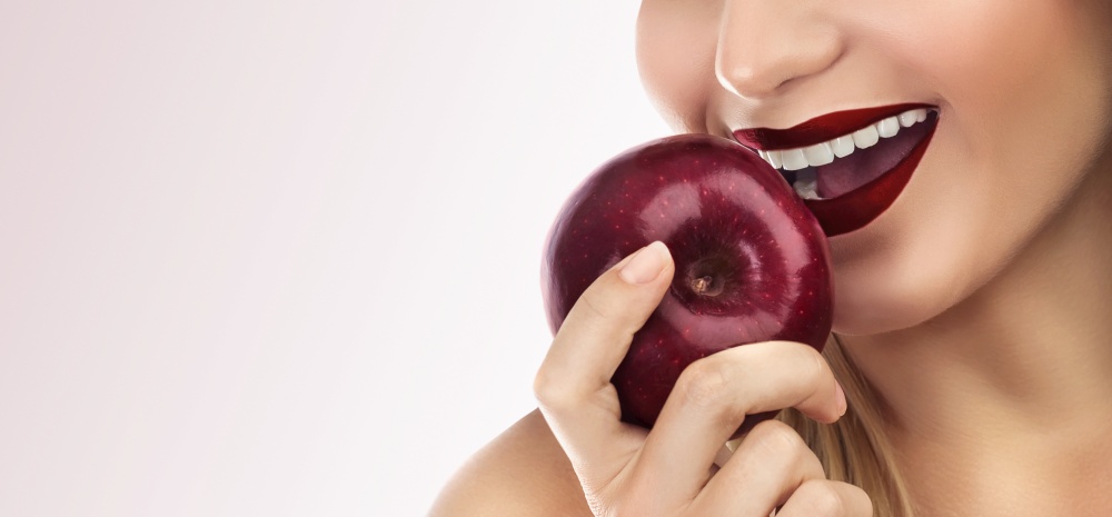 Closeup photo of a woman&rsquo;s face, lips with red lipstick, female biting  fresh red apple, isolated on a clean background, beautiful smile with perfect white teeth, dental care concept