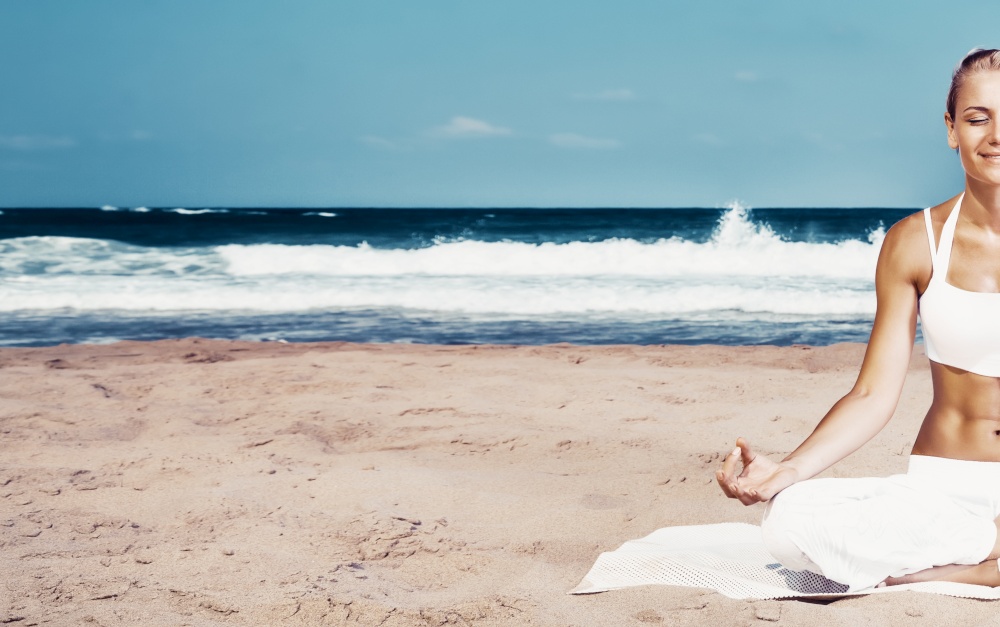 Pretty woman with pleasure meditating outdoors, sitting on the beach in lotus pose with closed eyes and doing yoga asana, photo of a half body, peace and zen balance concept