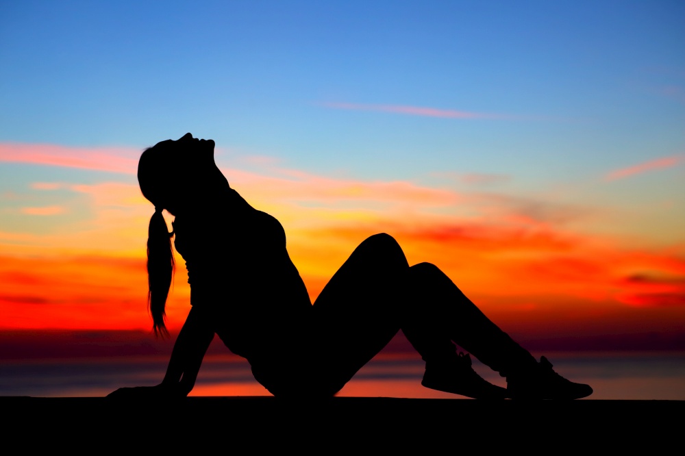 Silhouette of a woman sitting near the beach over beautiful colorful sunset background, enjoying beauty of evening nature, carefree summer holidays