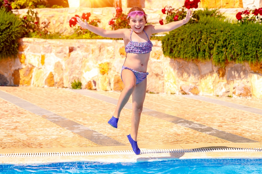 Joyful girl jumping to the pool, cute little child wearing goggles and flippers for diving, happy carefree childhood, enjoying summer holidays on the beach resort
