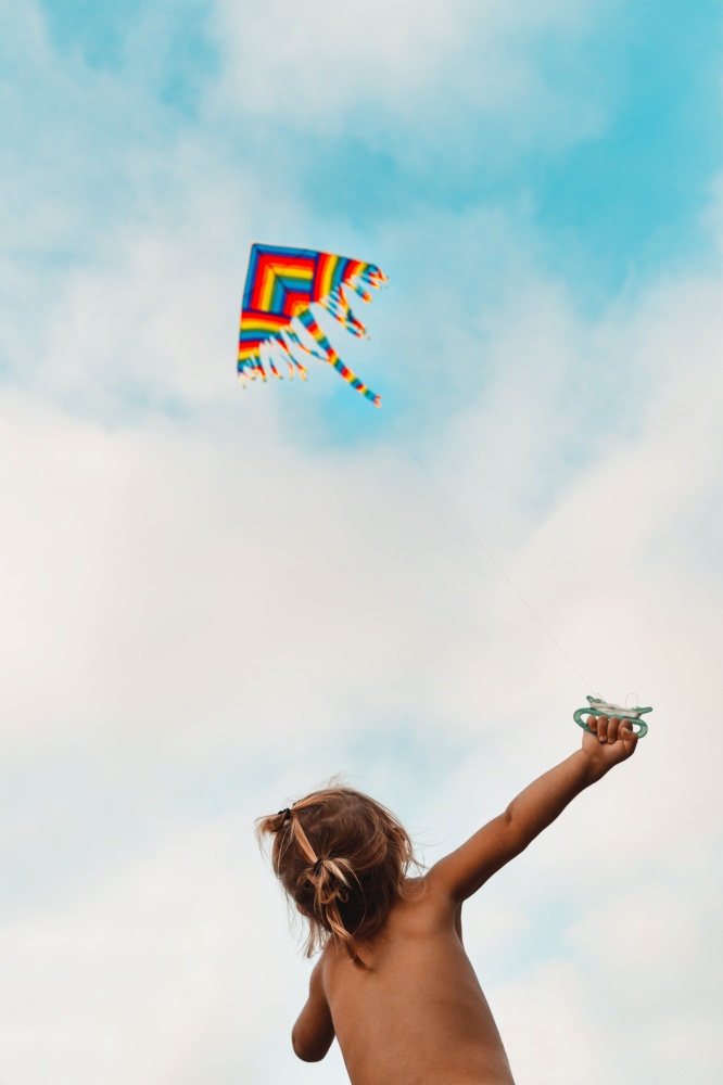 Happy child launches a kite, baby looking up at a multi-colored kite soaring in the sky, happy childhood, kid enjoying summer holidays, photo with copy space, freedom concept