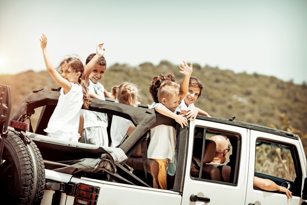 Happy kids enjoying road trip in the open-top 4x4, cheerful boys and girls having fun in the car riding along mountains, happy active summer holidays