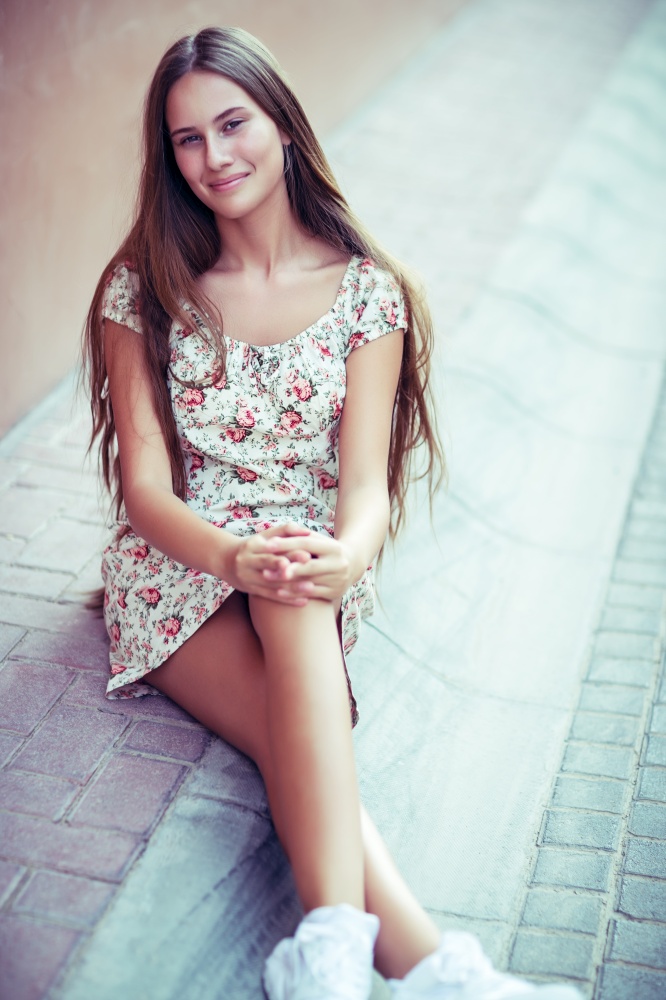 Portrait of a pretty brunette girl sitting on the street, nice attractive model with natural long hair, authentic young woman