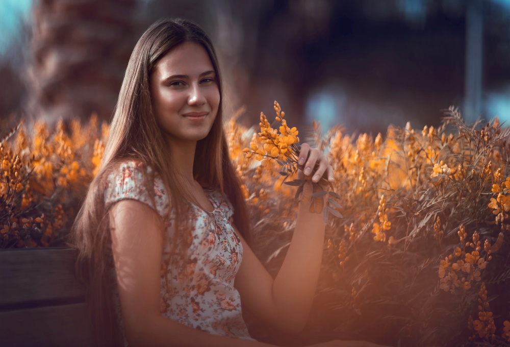 Portrait of a nice teen girl sitting on the bench in a floral garden, enjoying amazing beauty of a little gentle yellow flowers, freshness of spring nature