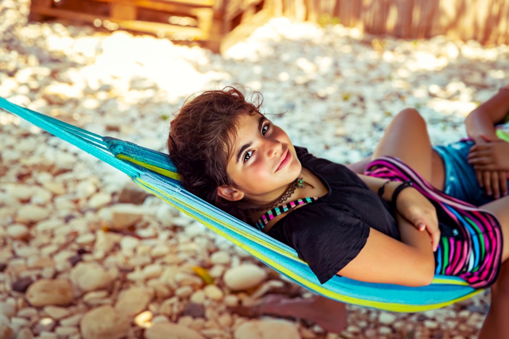 Little girl chilling out in hammock on the beach, with pleasure spending time near the sea, enjoying happy active summer vacation