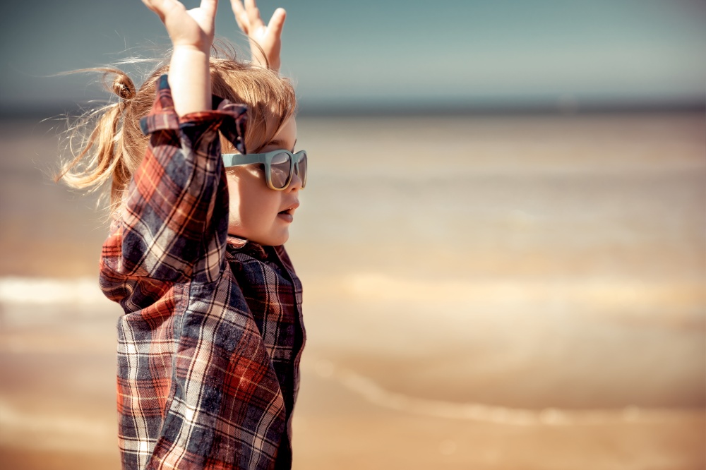 Cute joyful little boy having fun on the beach, adorable child with raised up hands running along seashore, active happy summer holidays