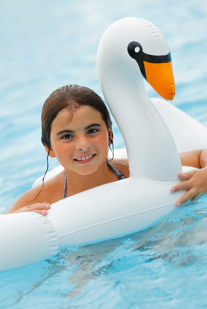Portrait of a Cheerful Little Girl Having Fun in the Swimming Pool. Young Pretty Lady with Pleasure Floating on the Rubber Ring in Swan Shape. Happy Summer Day in the Aqua park.