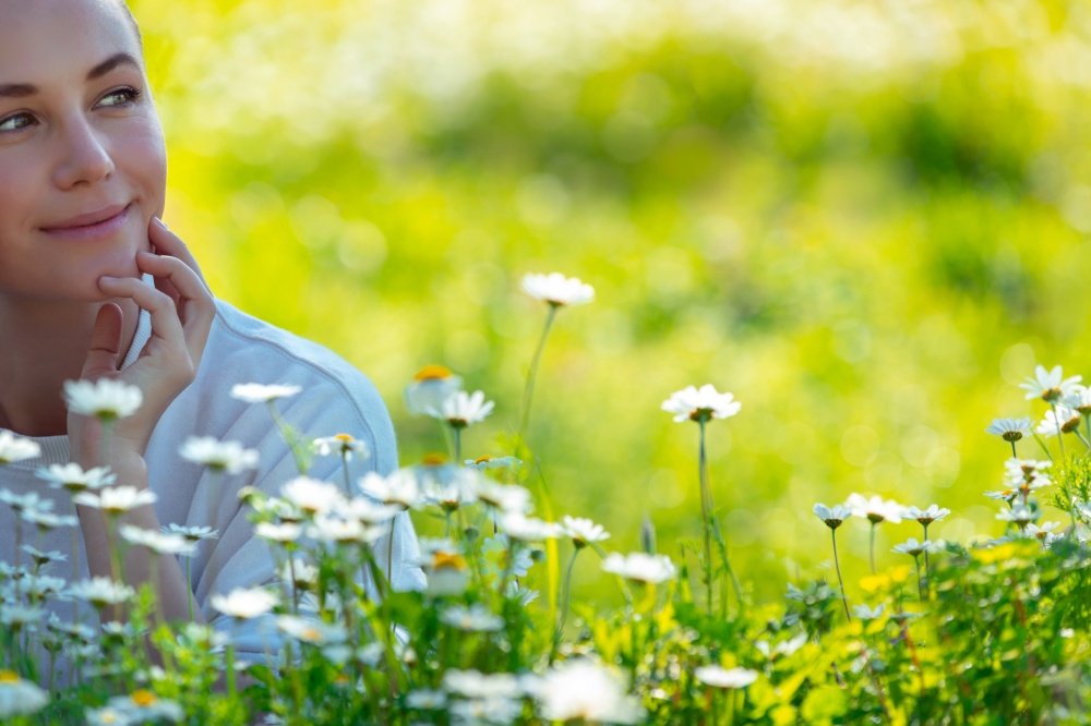 Young woman lying down on the fresh green grass among little gentle daisy flowers and daydreaming, enjoying beauty and freshness of spring nature
