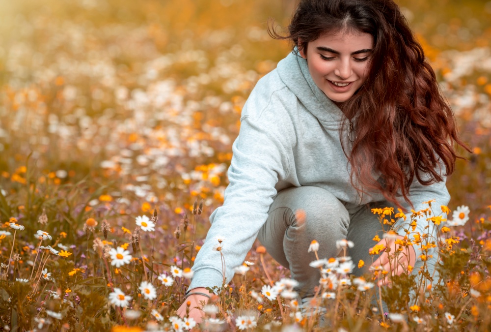 Teenager enjoying springtime holidays in the countryside, happy nice girl with pleasure picking little daisy flowers, spending quality time outdoors, breathing fresh air