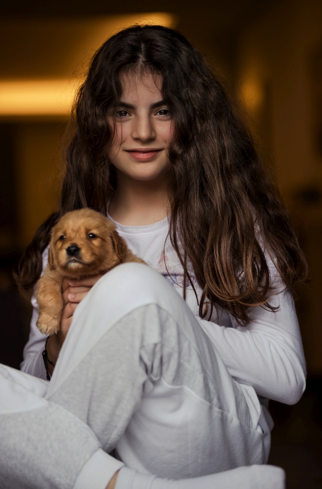 Portrait of a cute little girl holding in hands her new fluffy friend, cub of a golden retriever, happy best friends having fun together at home