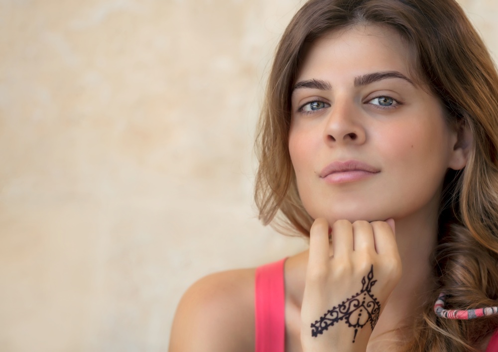 Portrait of an Attractive Woman Isolated on Beige Background with Beautiful Mehndi Drawing on the Hand. Stylish Body Art. Natural Beauty of Young Female. Photo with Copy Space.