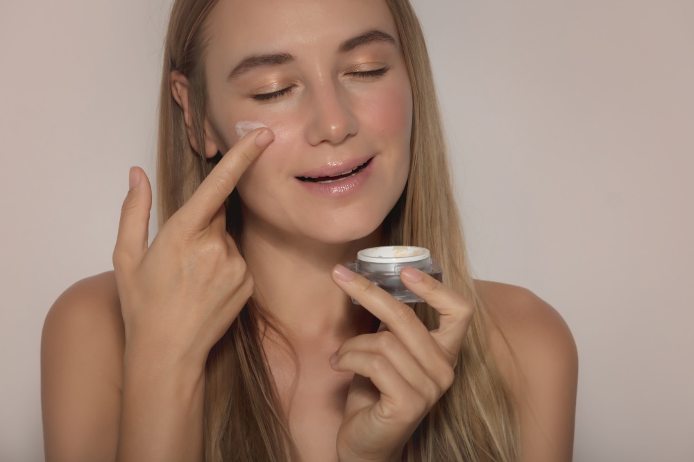 Portrait of a Beautiful Woman with Closed Eyes Applying Facial Moisturizer Cream. Natural Cosmetics. Isolated on Beige Background. Beauty Treatment. Healthy Lifestyle.. Beauty and Skin Care