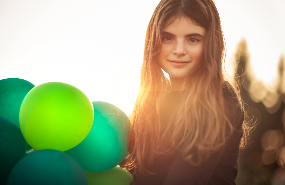Portrait of a cute girl with air balloons outdoors in mild evening sun light, celebrating birthday, holidays and fun concept