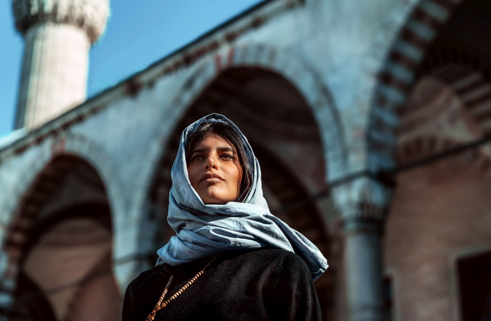 Closeup photo of an attractive arabic woman standing near mosque with covered head by stylish scarf, arabian fashion