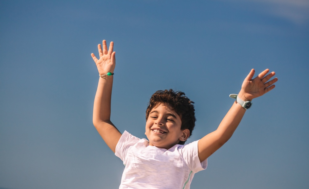 Happy Little Boy With Raised up Hands Having Fun Outdoors. Nice Child with Joy Spending Holidays in Summer Camp. Happiness and Freedom Concept.. Baby Boy Outdoors