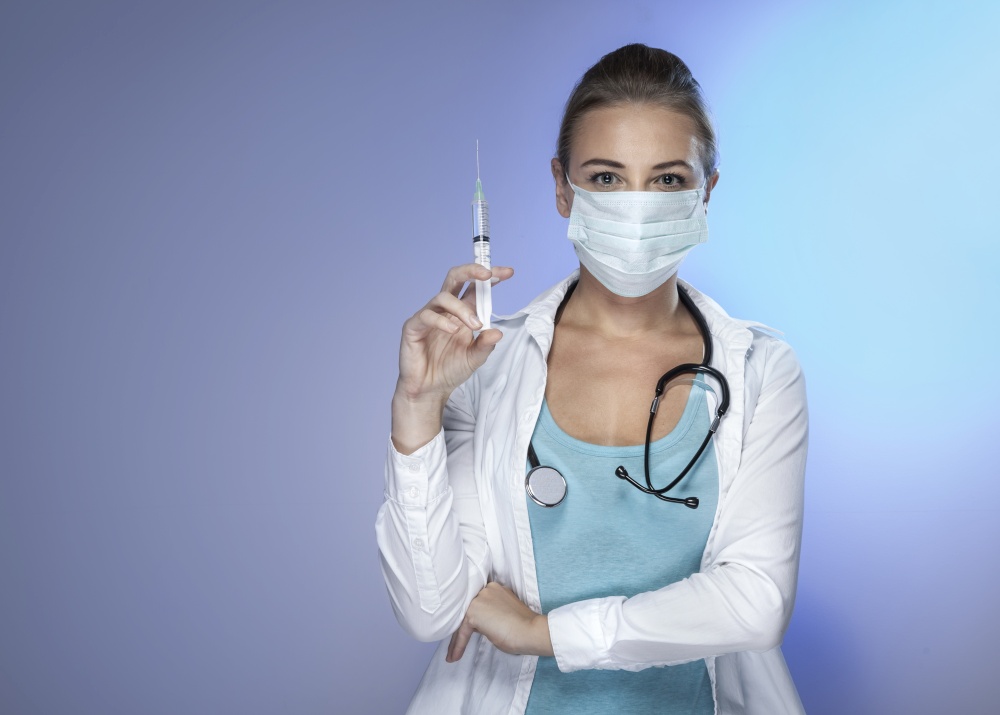 Portrait of a Serious Confident Doctor Woman with an Syringe isolated on Blue Background. Vaccination and Antiviral Injection Concept. Copy Space.. Doctor with an Injector