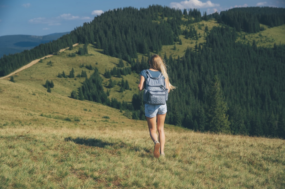 Rear View of a Woman with Backpack Walking in Carpathian Mountains. Traveling along Fresh Mountainous Forest. Active Life. Happy Summer. Ukraine. Traveler Girl in the Mountains