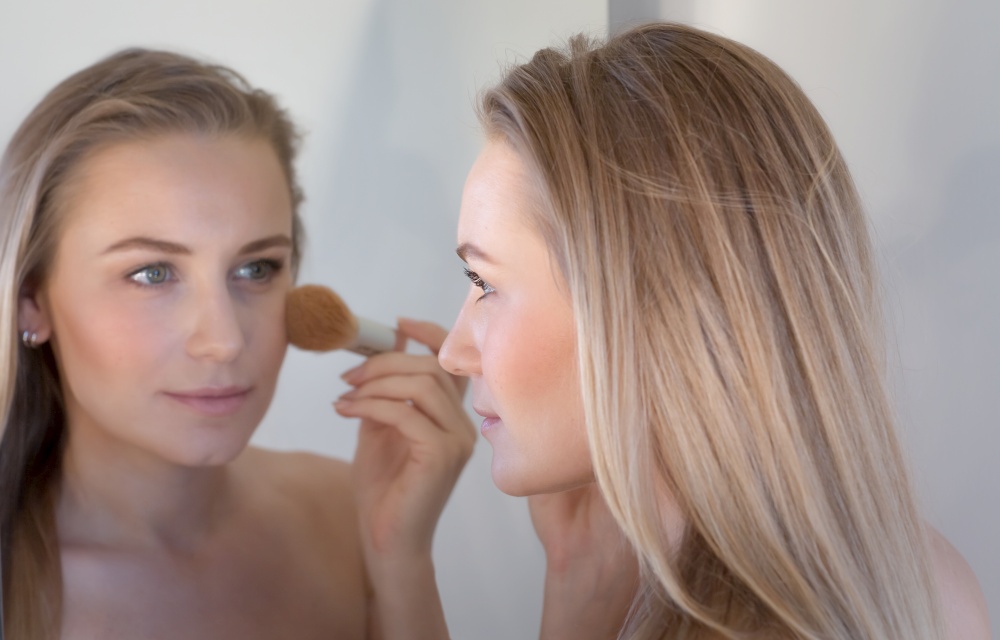 Closeup Portrait of an Attractive Blond Woman Doing Makeup near the Mirror. Applies Blush and Looks at her Reflection. Beauty of Young Female.. Woman Doing Makeup
