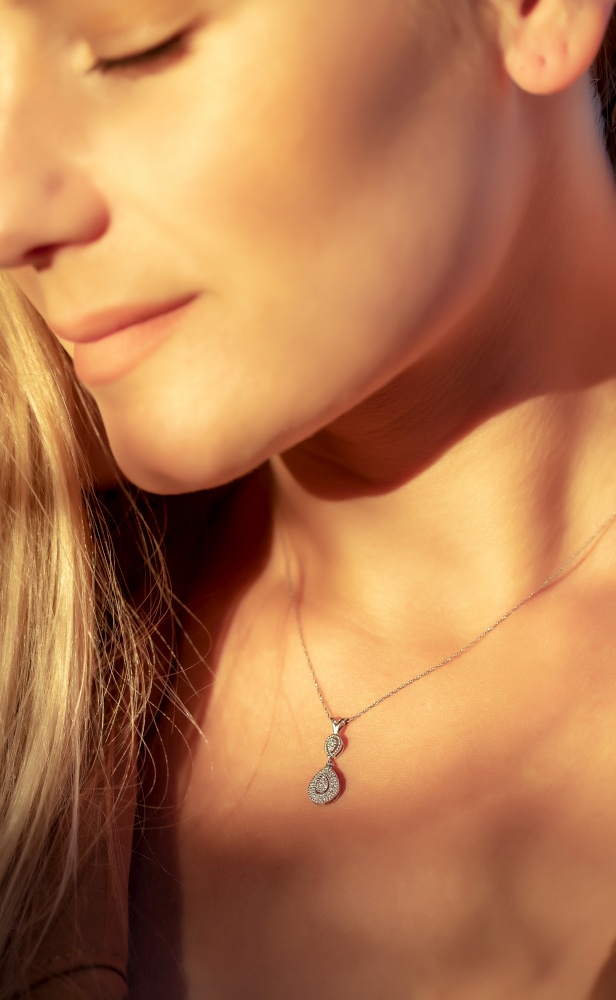 Woman with a Beautiful Pendant on her Neck in Mild Sunlight. Golden Chain with Little Precious Stone. Luxury Jewelry.. Girl with a Beautiful Pendant on her Neck