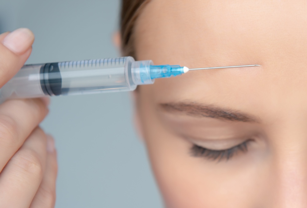 Closeup Photo of a Women&rsquo;s Face Part with Syringe near Forehead over Gray Background. Forehead Wrinkle Smoothing. Nice Female in a Beauty Clinic.. Forehead Wrinkle Smoothing