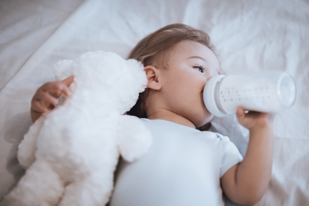 Portrait of a Cute Little Baby with Pleasure Drinking Formula Before Nap. Sleeping with Nice White Teddy Bear. Happy Healthy Childhood.. Sweet Baby Drinking Formula