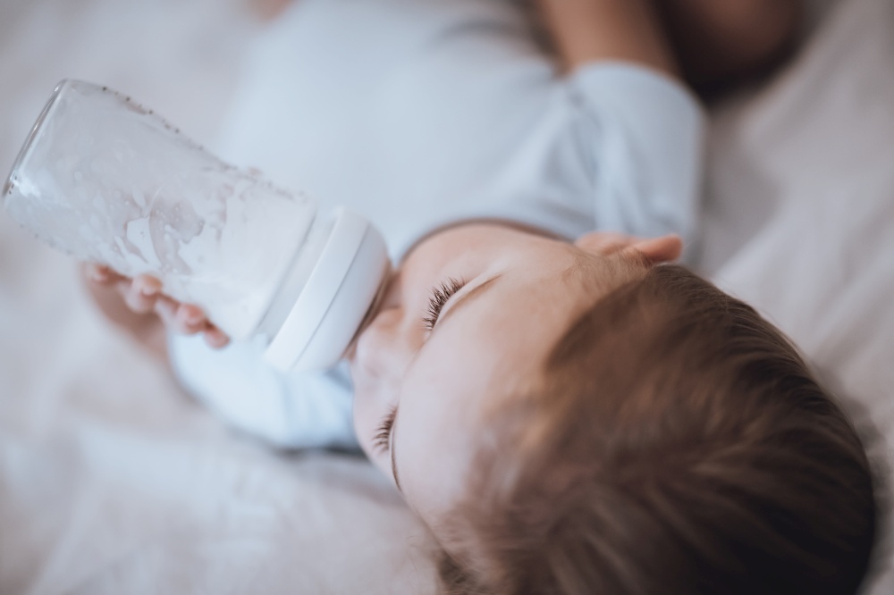 Portrait of a Nice Little Baby in the Bed Drinking Babies Food. Day Dreaming. Preparation for Sleep Time. Healthy Eating for Children.. Little Baby Eating