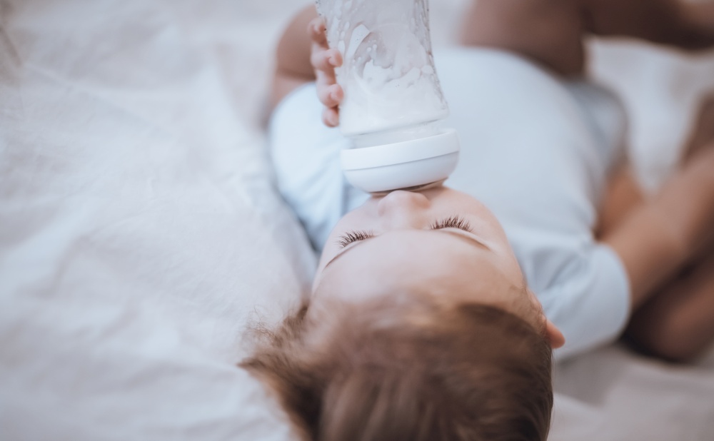 Portrait of a Cute Little Baby with Pleasure Drinking Formula Before Nap. Sleeping in Cute Child&rsquo;s Bedroom. Happy Healthy Childhood.. Sweet Baby Drinking Formula